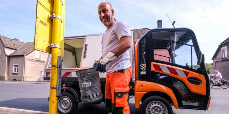 Ein Bauhofmitarbeiter leert einen Papierkorb an einer Haltestelle.