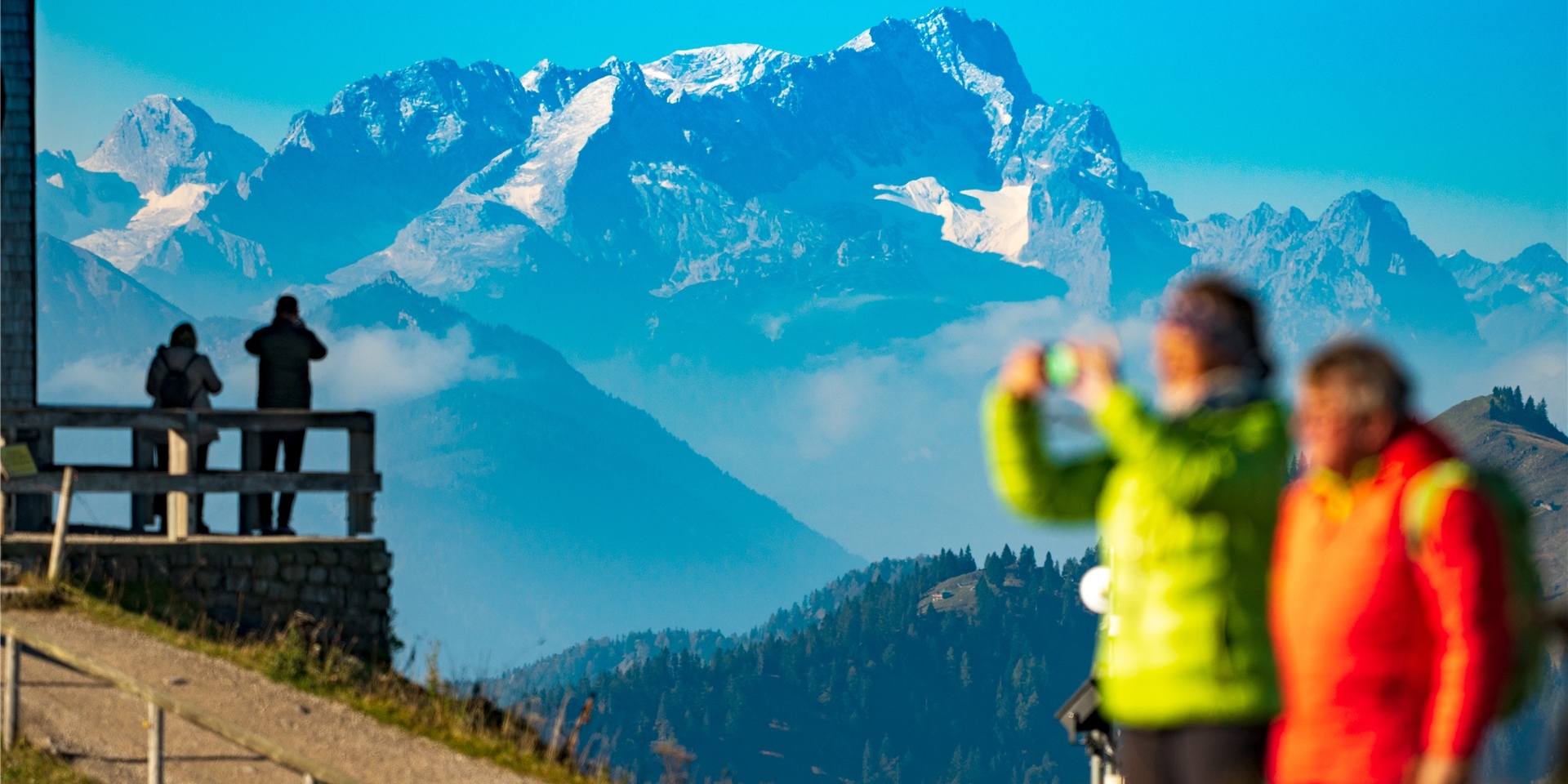 Besucher stehen in den Morgenstunden auf dem Wallberg vor der imposanten Kulisse der Zugspitze, die im Hintergrund in den Himmel ragt.