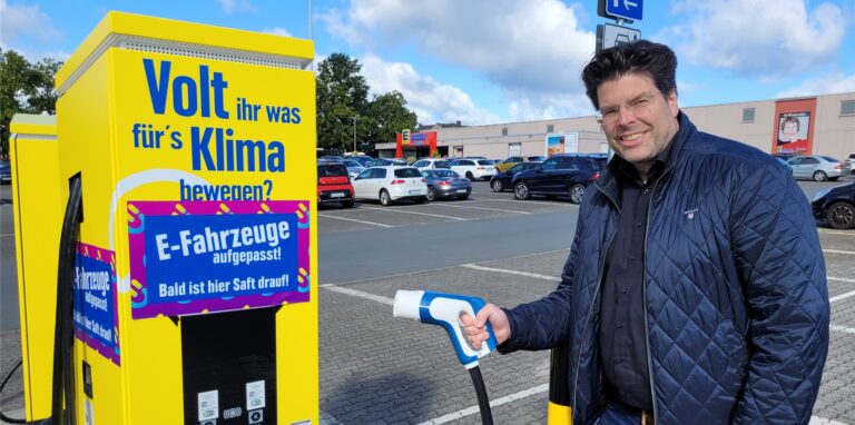 Edeka-Chef Marc Zierles steht vor einer gelben E-Ladesäule vor seinem Markt in Oer-Erkenschwick.