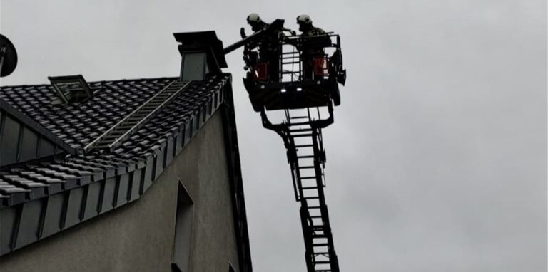 Feuerwehrleute reinigen einen brennenden Kamin von der Drehleiter aus.