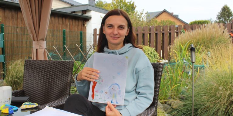 Eine Frau zeigt in einem Garten ein Kinderbild.