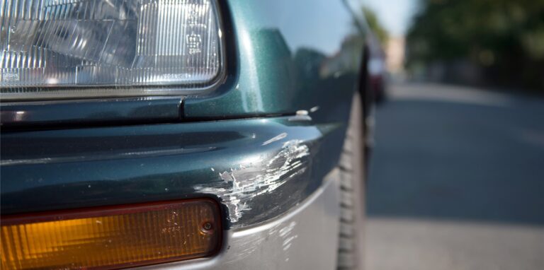 Am Stoßfänger eines geparkten Autos sind Spuren eines Unfalls zu sehen.