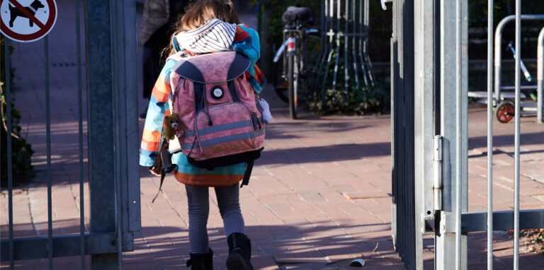 Ein Schulkind geht mit seinem Schulranzen durch das Eingangstor einer Schule.