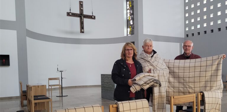 Martina Czarkowski und Petra Küper vom Kirchencafé und Organist Heinrich-Josef Schlathölter halten in einem Altarraum Decken für Gottesdienstbesucher in Oer-Erkenschwick bereit.