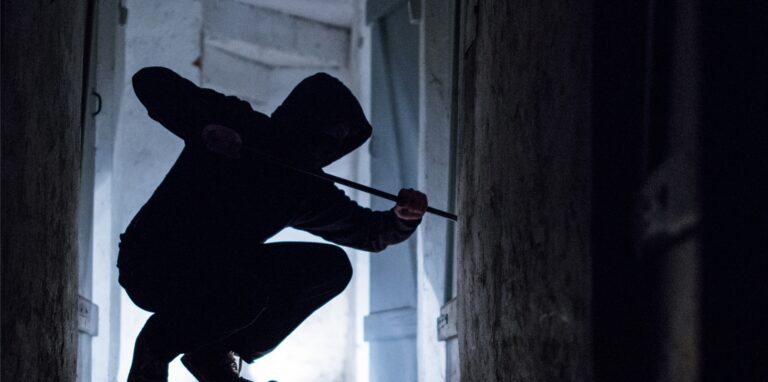 Ein Einbrecher hockt mit einem Brecheisen auf einer Fensterbank.