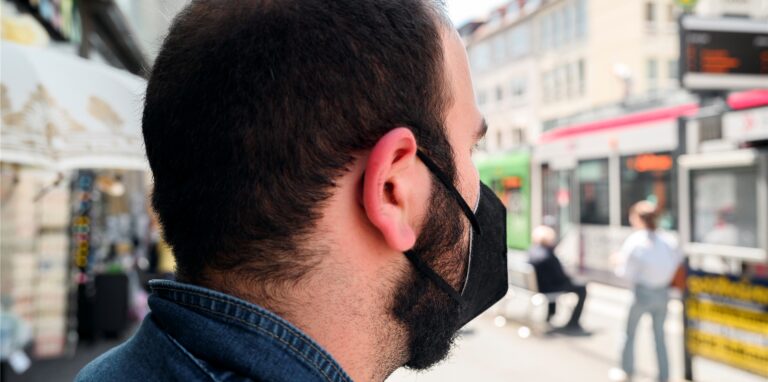 Ein Mann trägt an der Straßenbahnhaltestelle Dom eine FFP-2 Maske.