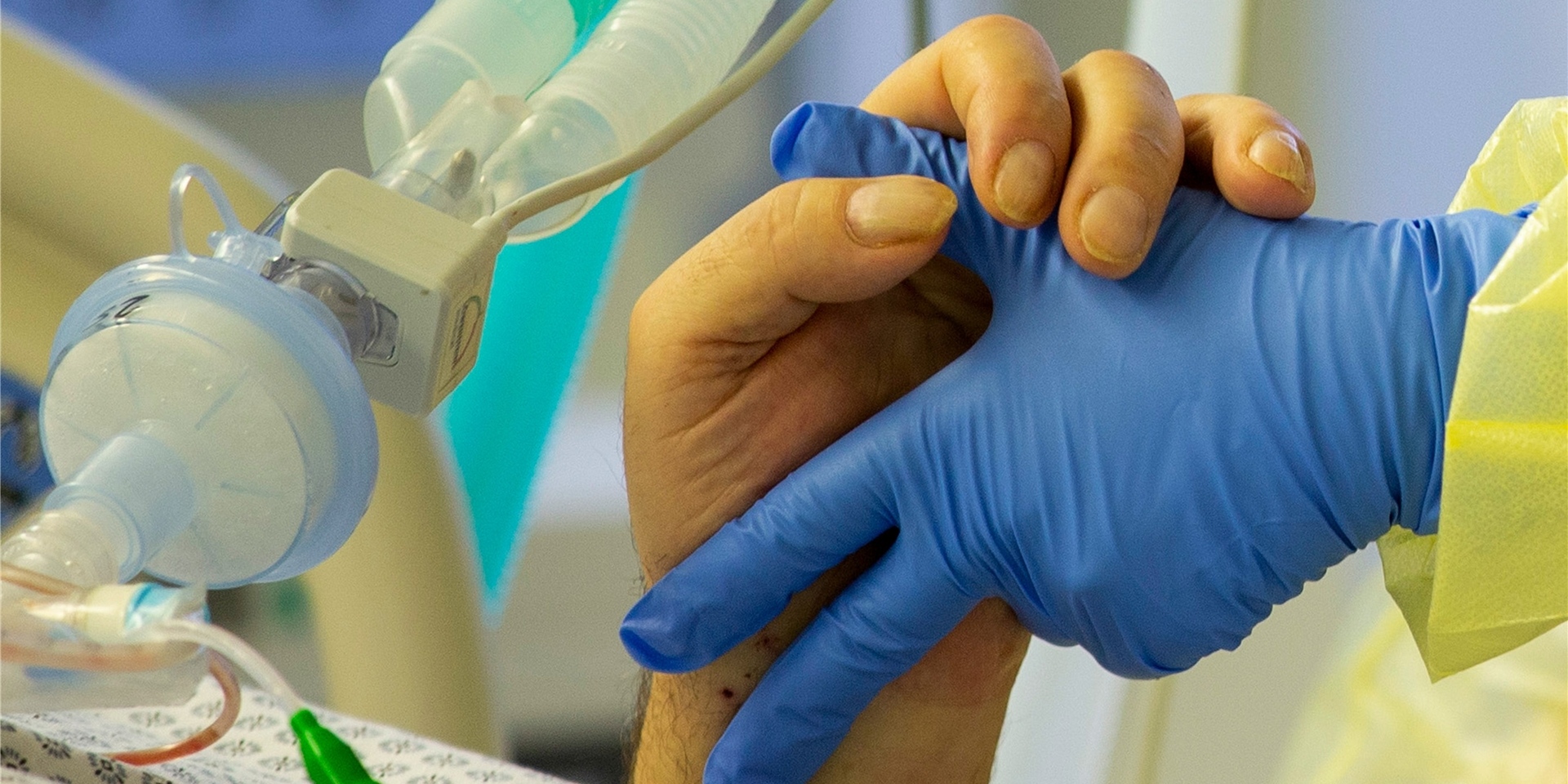 Ein Intensivpatient hält die Hand eines Krankenpflegers.