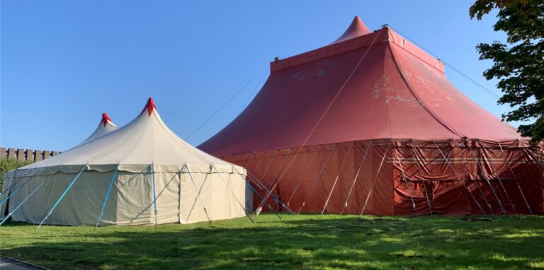 Auf der Wiese neben der Europahalle steht ein rotes Zirkuszelt sowie ein kleineres weißes Vorzelt.