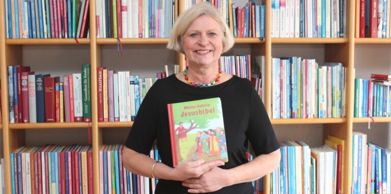 Die Waltroperin Cordula Janusch hat eine Kinderbibel geschrieben und steht mit einem Exemplar des Buches vor einer Bücherwand.