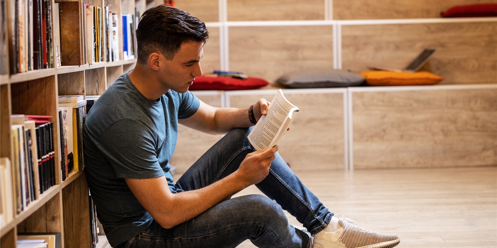 mann sitzt auf dem boden vor einem bücherregal und liest