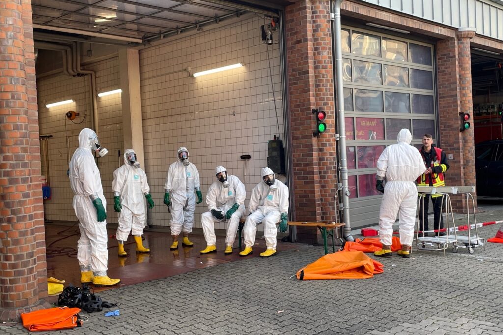 Einsatzkräfte in Schutzanzügen stehen an der Feuerwache in Herten-Mitte. Einsatzkräfte in Schutzanzügen stehen an der Feuerwache in Herten-Mitte.