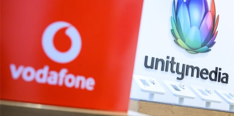 Eine Box mit dem Logo von Vodafone steht in einem Shop des Unternehmens vor einem Logo von Unitymedia.