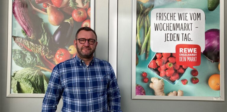 Rewe-Geschäftsführer Marcus Engelhardt aus Recklinghausen steht vor zwei Rewe-Plakaten.
