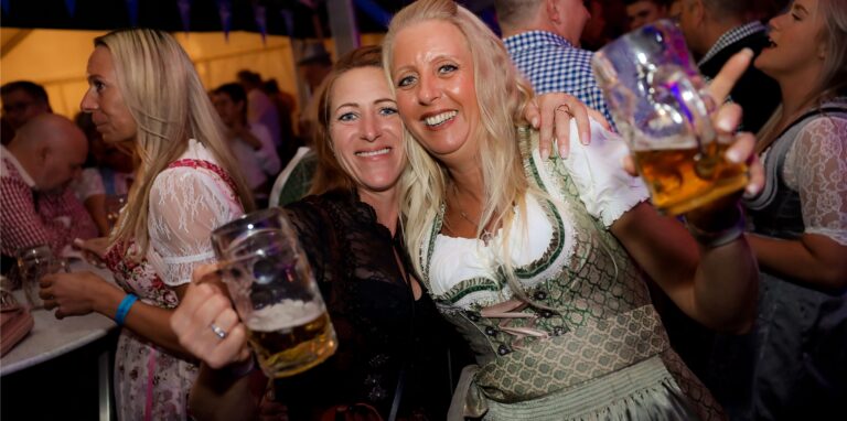 Zwei Frauen in Dirndl halten eine Maß Bier im Oktoberfest-Festzelt in der Feldmark in die Höhe.