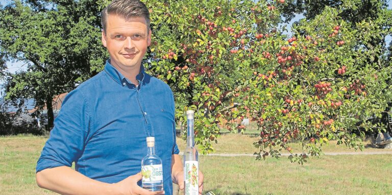Ein Mann steht vor einem Apfelbaum und hält zwei Flaschen.