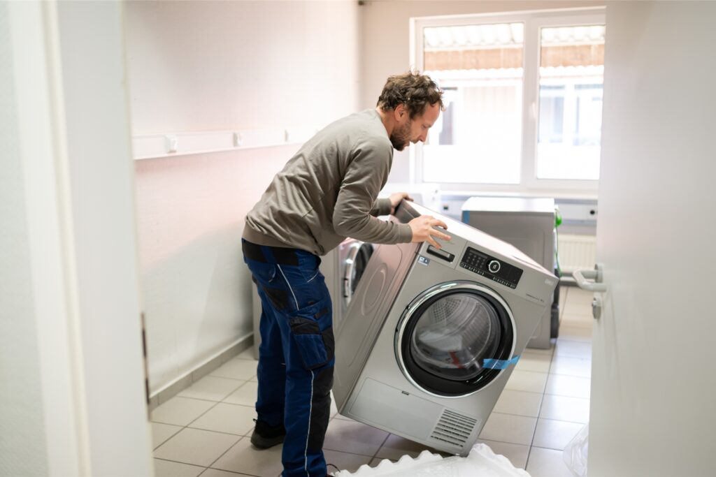 Ein Mann trägt eine Waschmaschine in einen Kellerraum