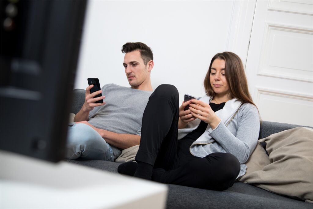 Ein Mann und eine Frau sitzen auf dem Sofa und surfen mit den Handys im Internet