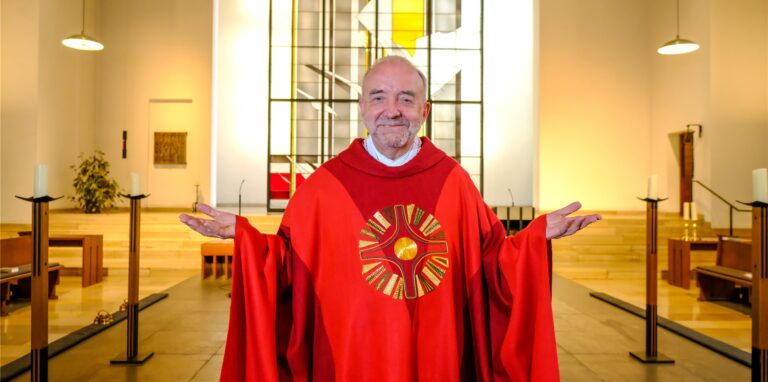 Pfarrer Aloys Wiggeringloh steht mit ausgebreiteten Armen und in rotem Talar in der Antonius-Kirche in Recklinghauen.