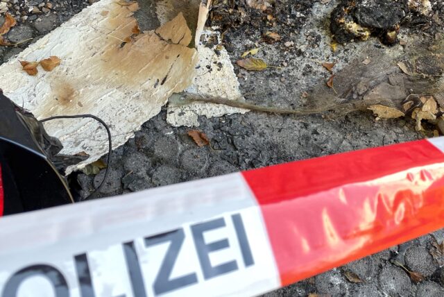 Flatterband der Polizei und ein geschmolzenes Rücklicht einer schwarzen Limousine. Im Hintergrund die Überreste des Brandanschlags an der Habinghorster Straße.