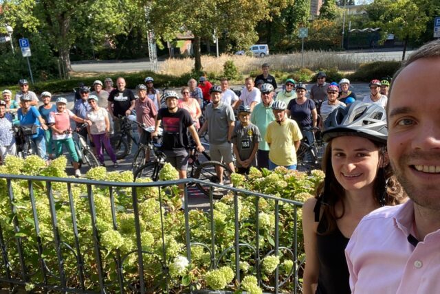 Waltrops Bürgermeister Marcel Mittelbach und die Klimaschutzmanagerin Nadine Schmidt stehen auf den Stufen des Rathauses, im Hintergrund diverse Teilnehmer einer Radtour.