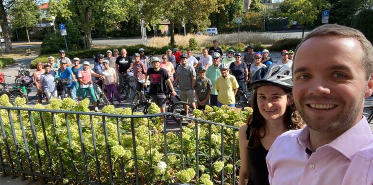 Waltrops Bürgermeister Marcel Mittelbach und die Klimaschutzmanagerin Nadine Schmidt stehen auf den Stufen des Rathauses, im Hintergrund diverse Teilnehmer einer Radtour.