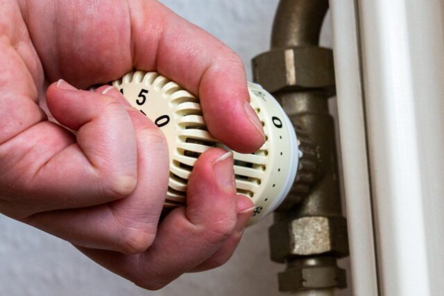 Eine Person dreht am Thermostat einer Heizung in einer Wohnung.