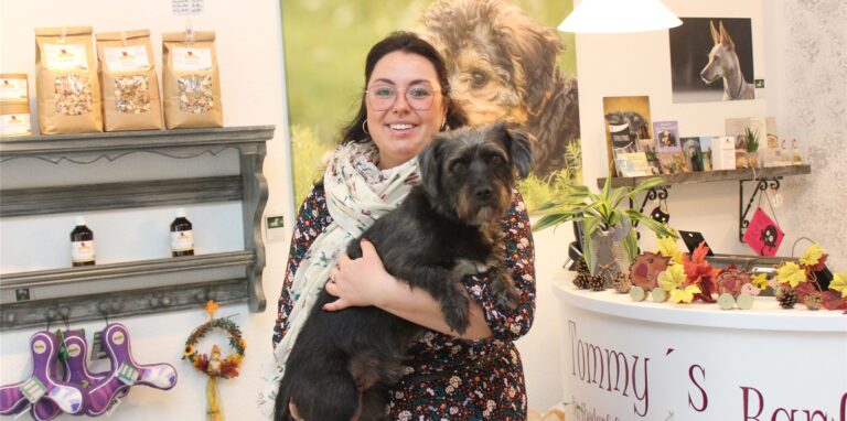 Jana Große hat ihren Hund Baloo auf dem Arm und steht in ihrem Laden, Tommys Barfshop in Waltrop.