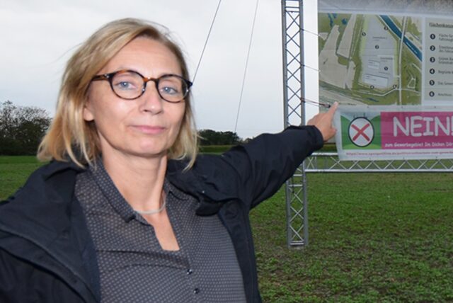 Aktionsbündnis-Srecherin Stefanie Hugot zeigt auf ein Transparent mit den Plänen für das Industriegebiet.