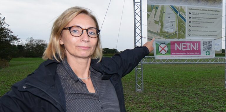 Aktionsbündnis-Srecherin Stefanie Hugot zeigt auf ein Transparent mit den Plänen für das Industriegebiet.