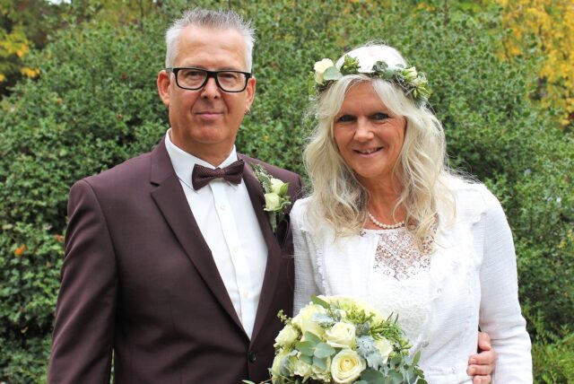 Das Brautpaar Iris Ehrhardt und Bernd Zahler steht vor einem Gebüsch am Waltroper Rathaus.