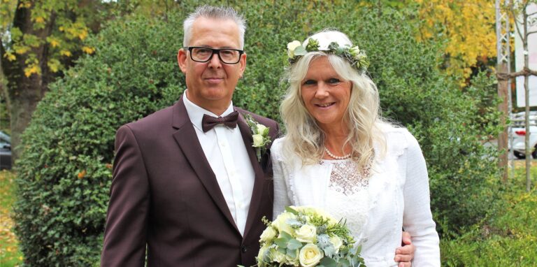 Das Brautpaar Iris Ehrhardt und Bernd Zahler steht vor einem Gebüsch am Waltroper Rathaus.