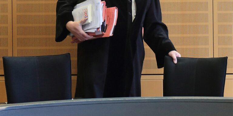 Ein Richter rückt sich in einem Verhandlungssaal seinen Stuhl zurecht.