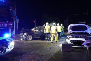 Mitten auf der Kreuzung stehen zwei Autos mit Unfallspuren. Feuerwehrleute und ein -fahrzeug stehen ebenfalls auf der Kreuzung.