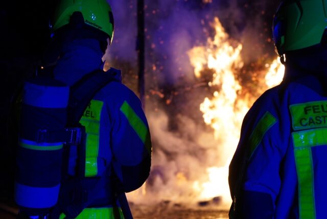 Zwei Einsatzkräfte der Feuerwehr Castrop-Rauxel stehen vor einer brennenden Mülltonne.