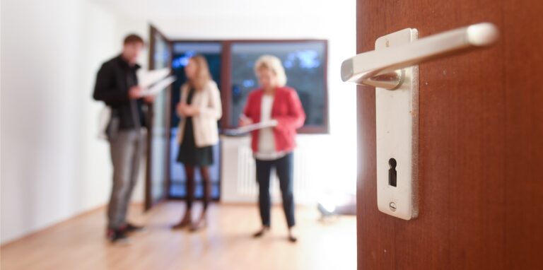 Eine Maklerin spricht mit Interessenten bei einer Wohnungsbesichtigung während im Vordergrund eine Türklinke zu sehen ist. Mietwohnungen werden auch in Oer-Erkenschwick zur Mangelware.