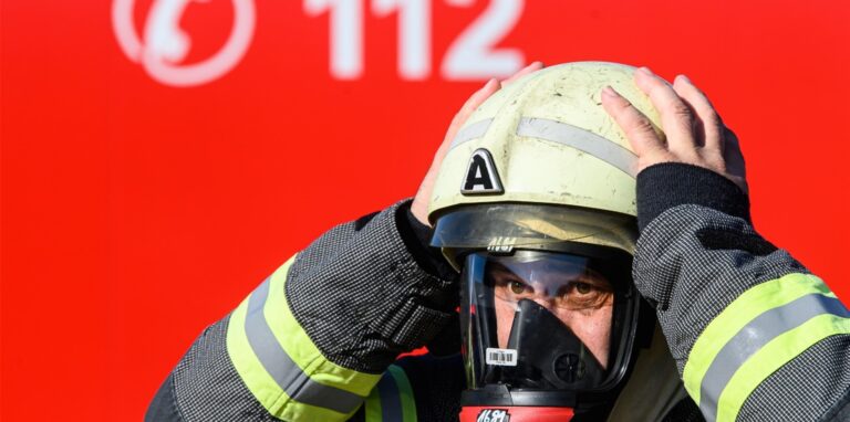 Ein Feuerwehrmann mit Atemschutzmaske packt sich mit beiden Händen an den Helm. (Symbolbild)