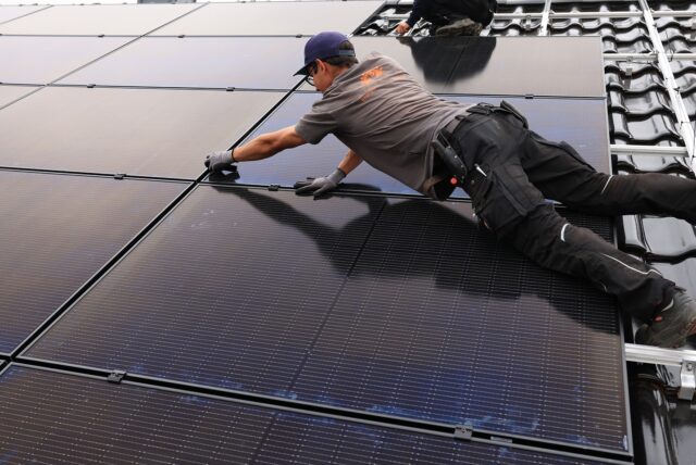 Handwerker montieren auf dem Dach eines Wohnhauses Solarmodule.