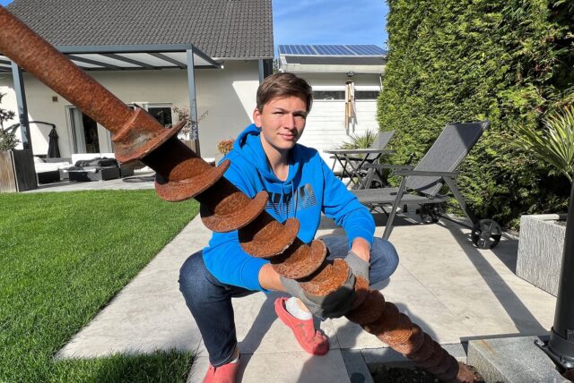 Jonas Kalla steht mit einem Bohrgestänge in seinem Garten.