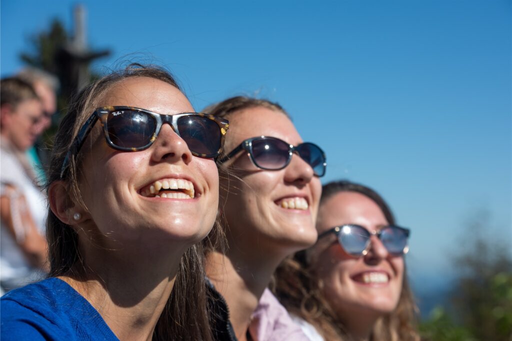 Drei Frauen mit Sonnenbrillen schauen in die Sonne.
