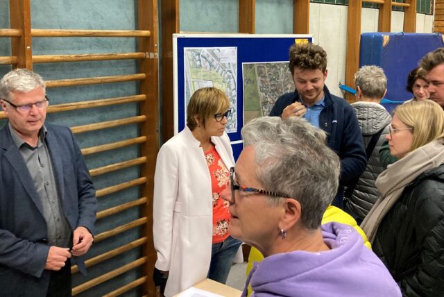 Stadtplanungsamtsleiter Markus Schaffrath (l.) und Baudezernentin Andrea Baudek (M.) diskutieren mit den anwesenden Bürgerinnen und Bürgern über die verschiedenen Varianten des Rewe-Feldmann-Umzugs.