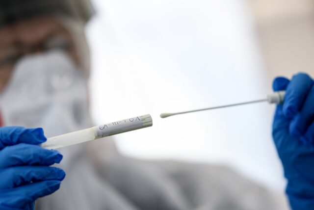 Ein Mann hält eine Coronatest-Ampulle in der Hand.