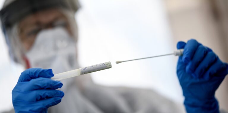 Ein Mann hält eine Coronatest-Ampulle in der Hand.