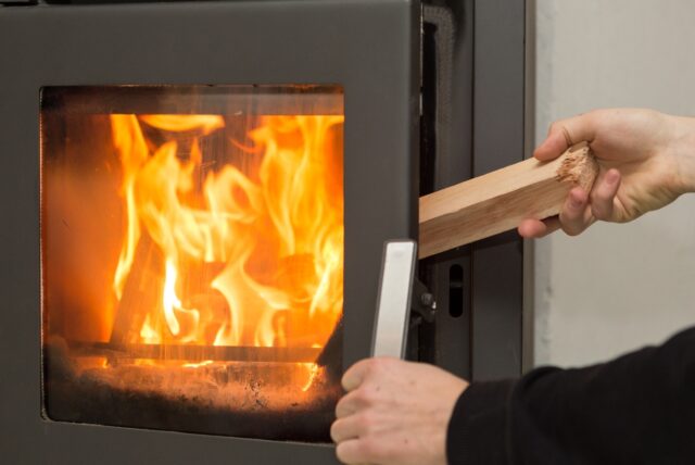 Eine Person legt ein Stück Holz in einen Kaminofen