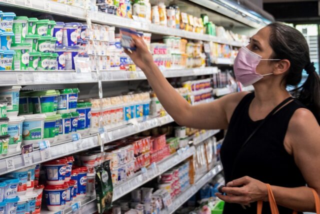 Eine Frau mit Mund-Nasen-Bedeckung steht vor einem Kühlregal im Supermarkt.