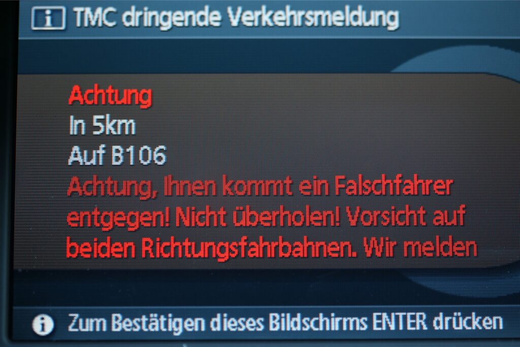 Auf dem Display eines Navigationssystems ist eine dringende Verkehrsmeldung zu einem Falschfahrer zu sehen.