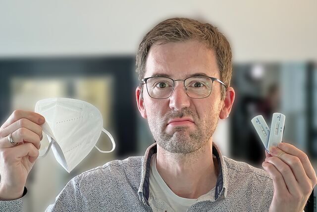 Papatastisch-Autor Thomas Raulf zeigt eine FFP-2-Maske und zwei Corona-Selbsttests