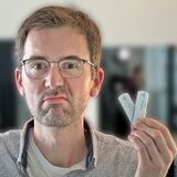 Papatastisch-Autor Thomas Raulf zeigt eine FFP-2-Maske und zwei Corona-Selbsttests