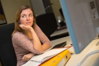 Eine Frau sitzt am Schreibtisch und schaut zur Seite.