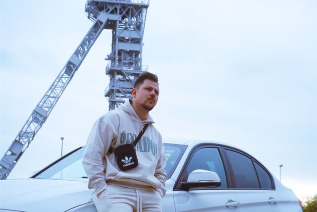 Alexander Büning sitzt auf einer Auto-Motorhaube vor einem Zechenturm.