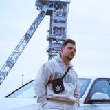 Alexander Büning sitzt auf einer Auto-Motorhaube vor einem Zechenturm.